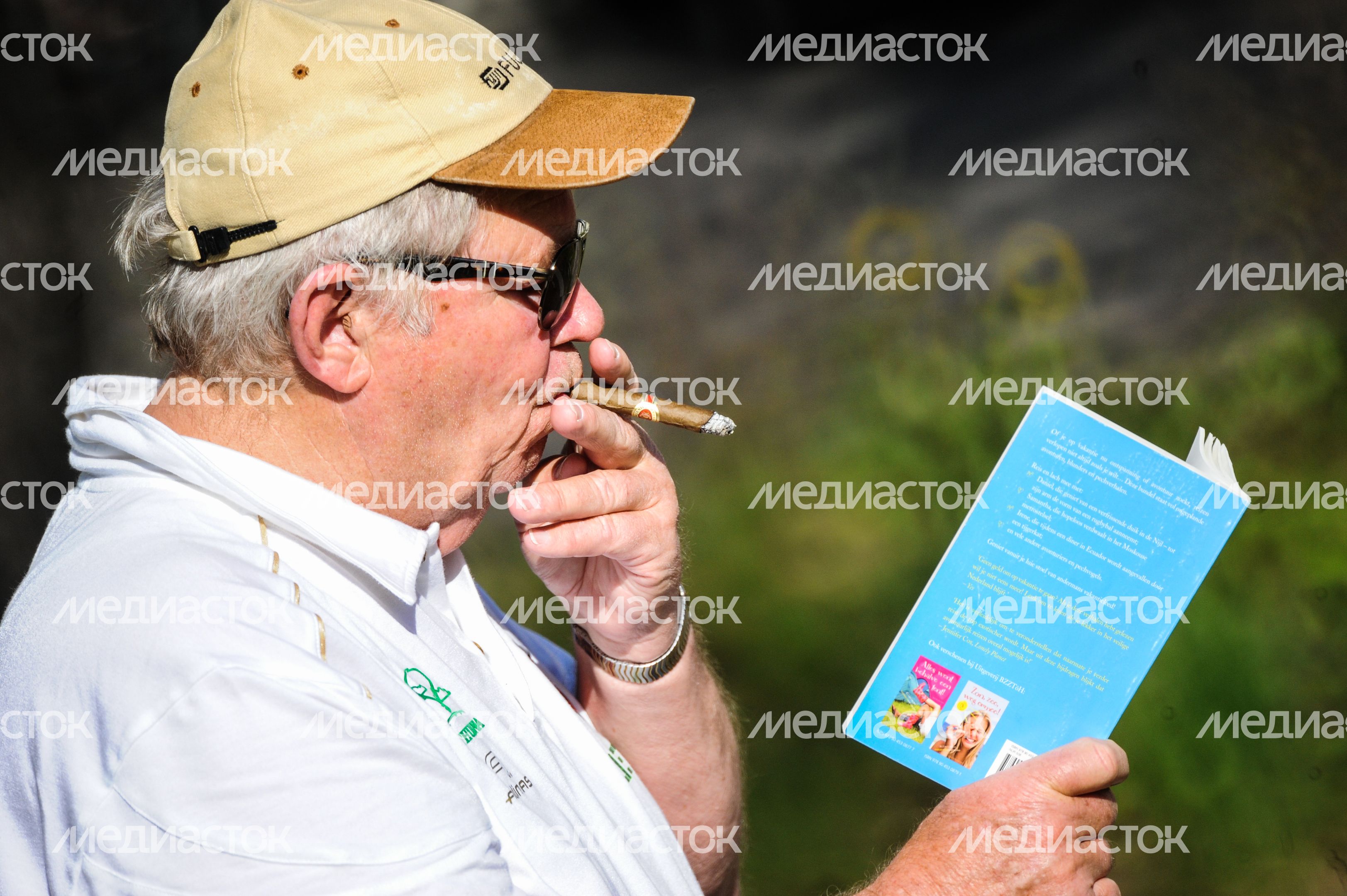 Мужчина курит сигару и читает книгу Мужчина курит сигару и читает книгу
